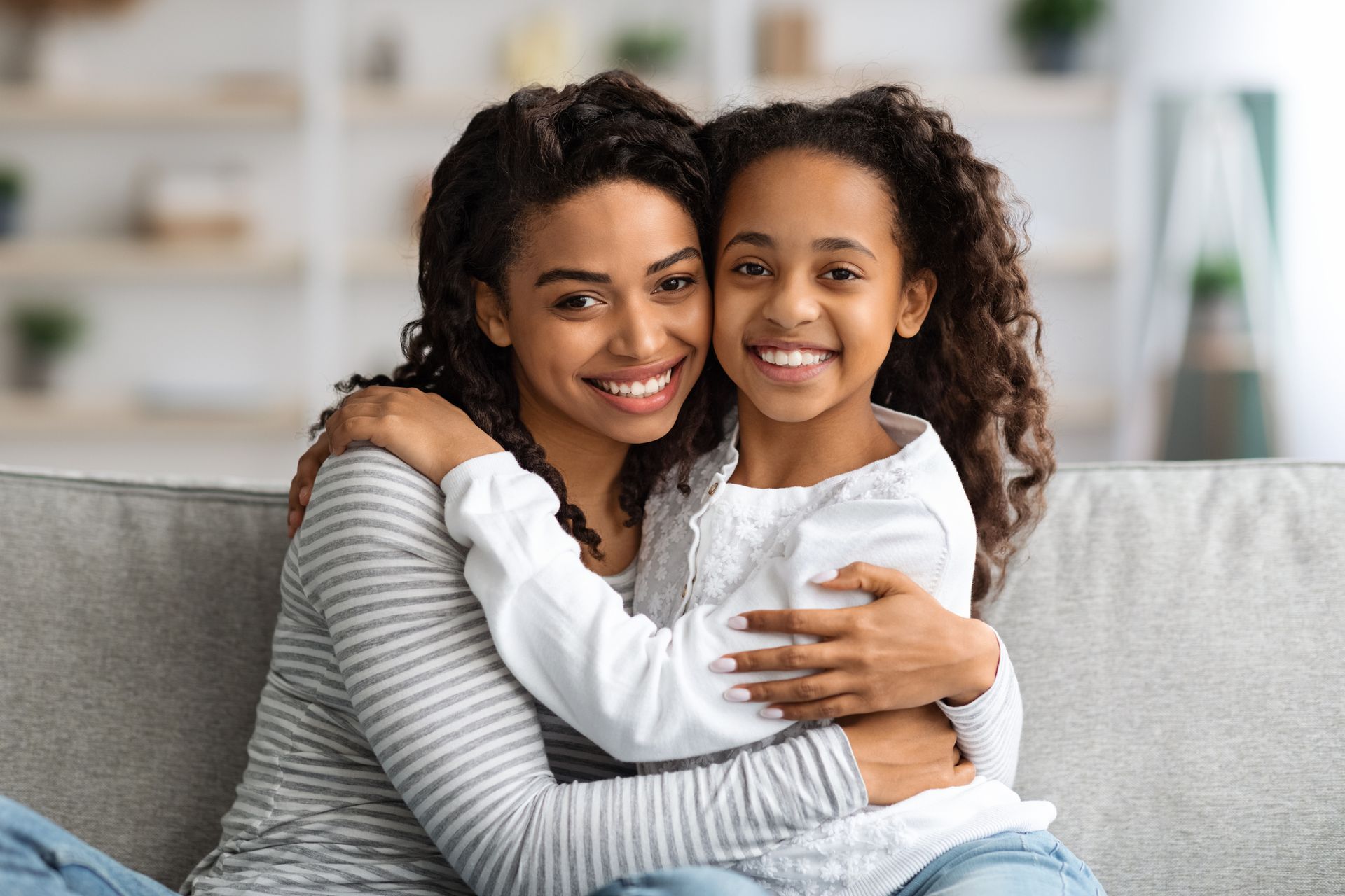 A mother and daughter are hugging each other while sitting on a couch.