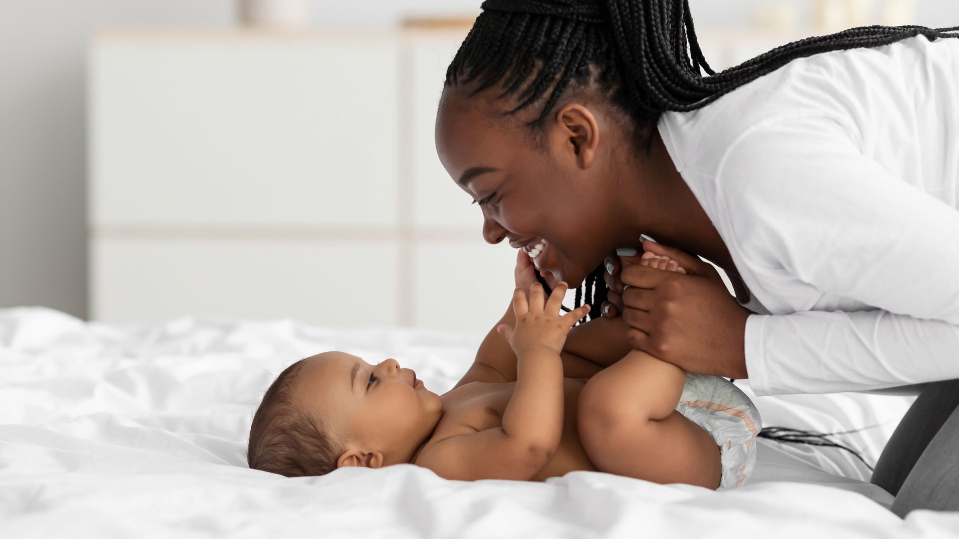 A woman is playing with her baby on a bed.