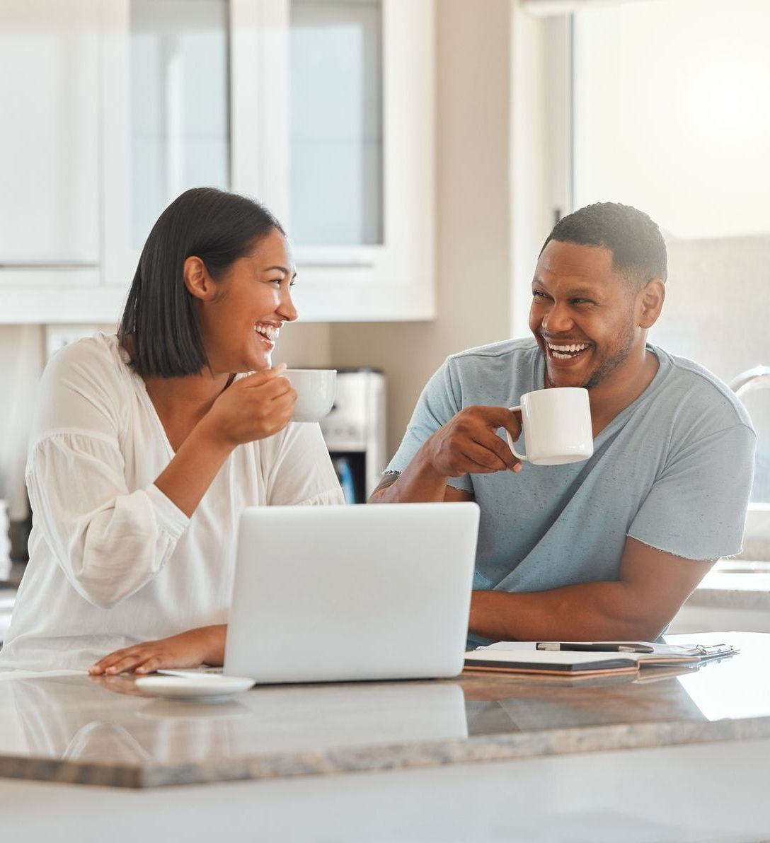 A man and a woman are sitting at a table with a laptop and drinking coffee.