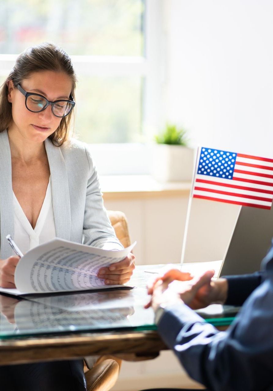 A woman is sitting at a table with a laptop and an American flag.