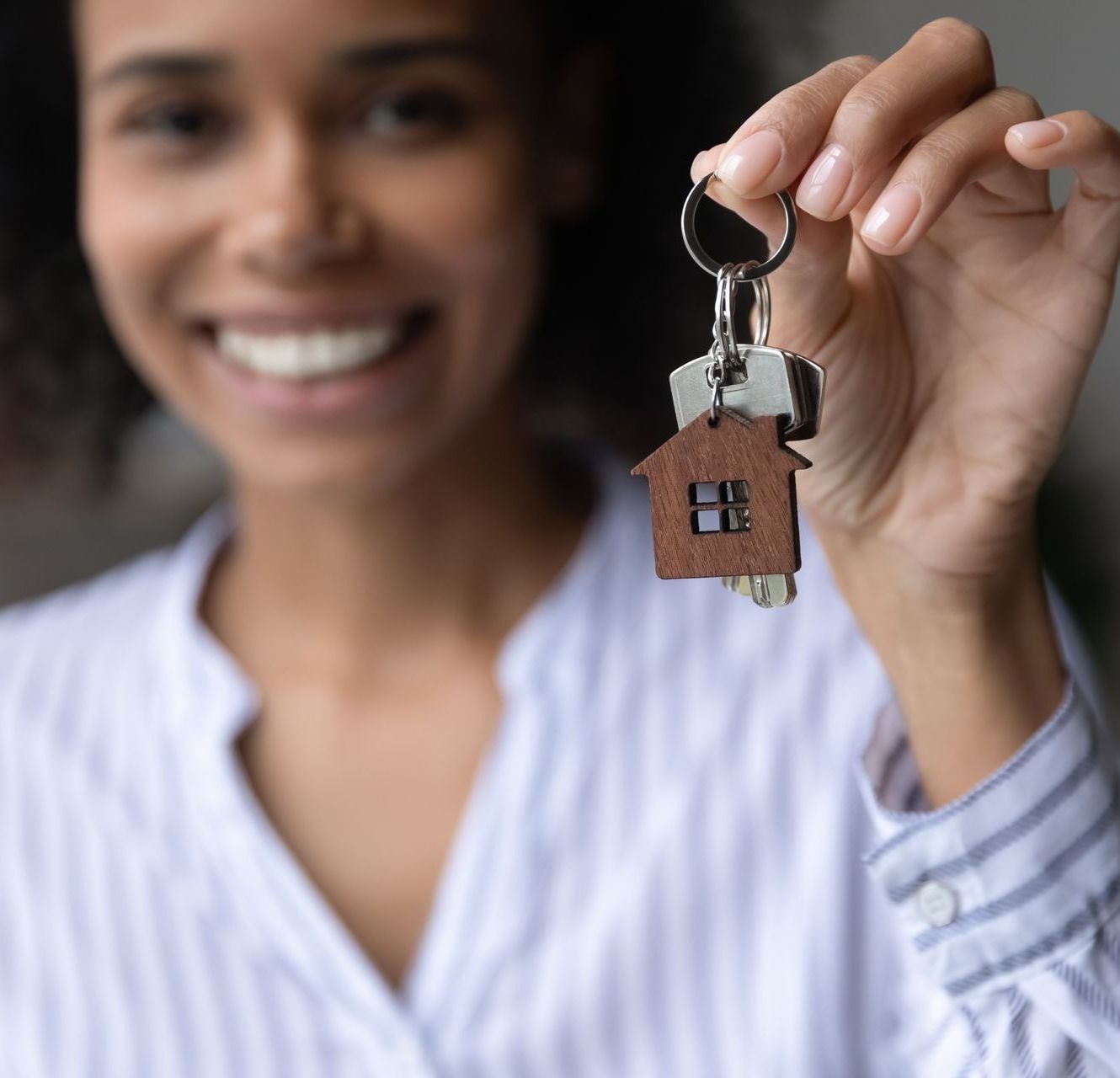 A woman is holding a pair of keys with a house keychain attached to them.