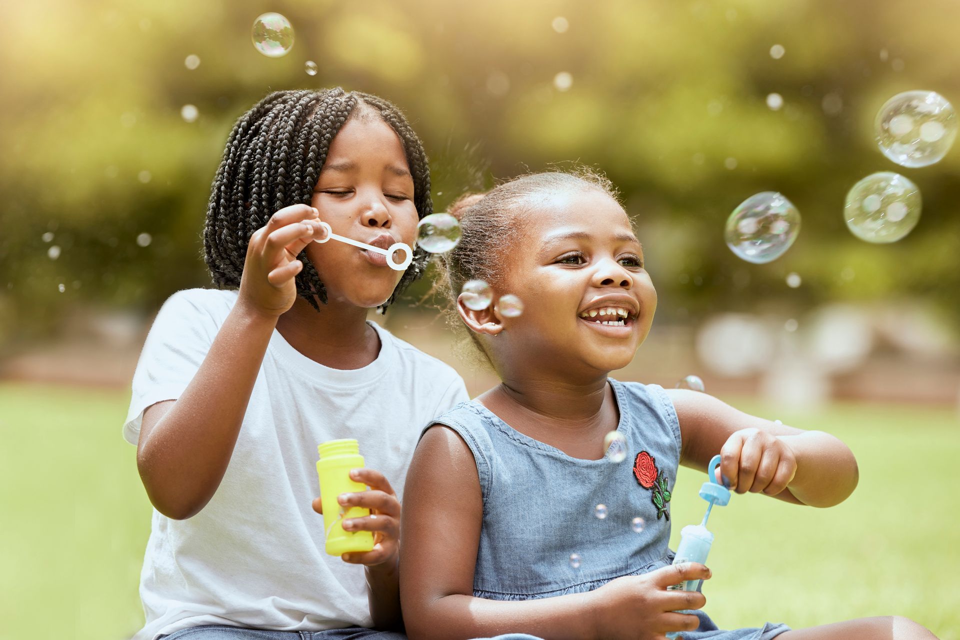 two little girls are blowing soap bubbles in a park .