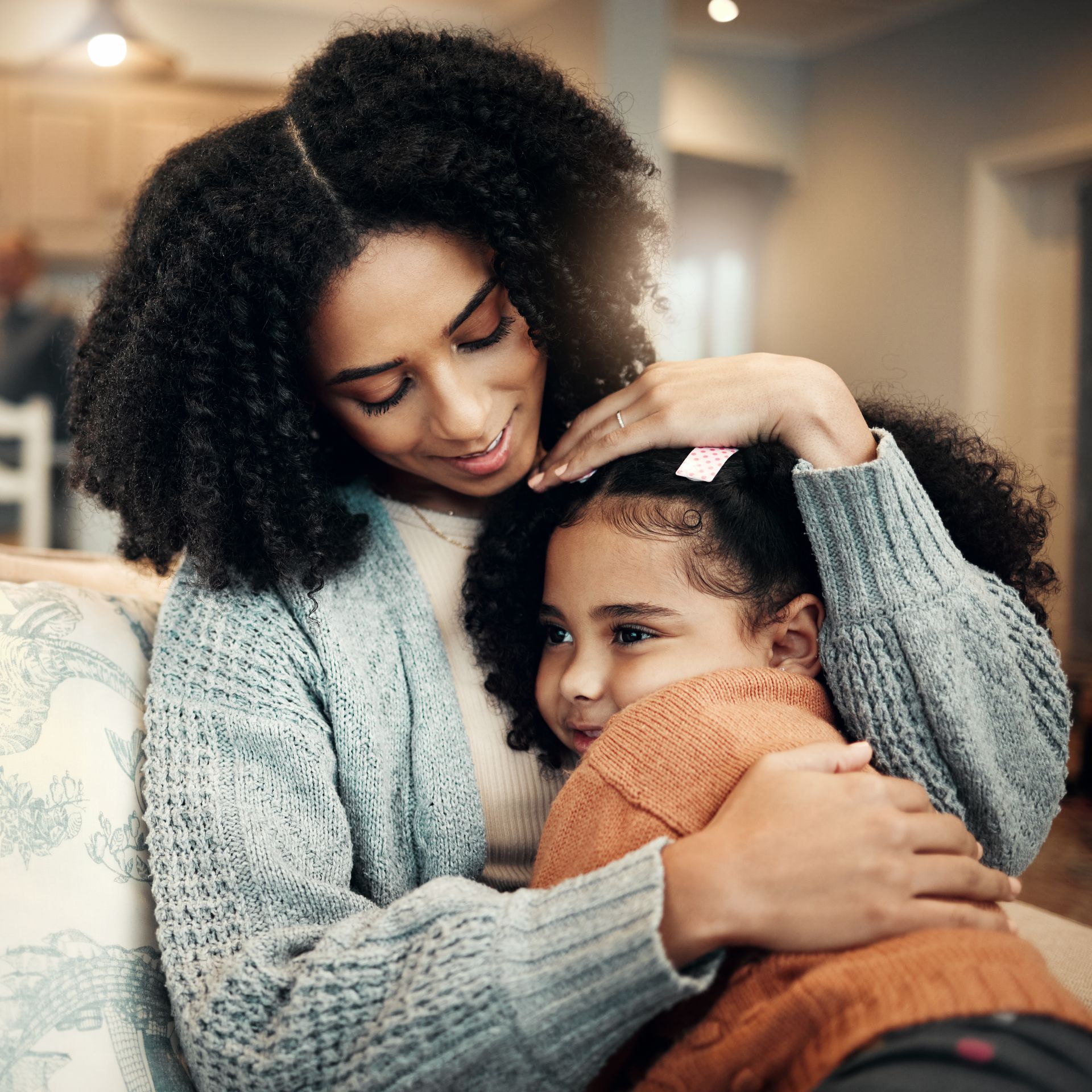 A woman is hugging a little girl on a couch.