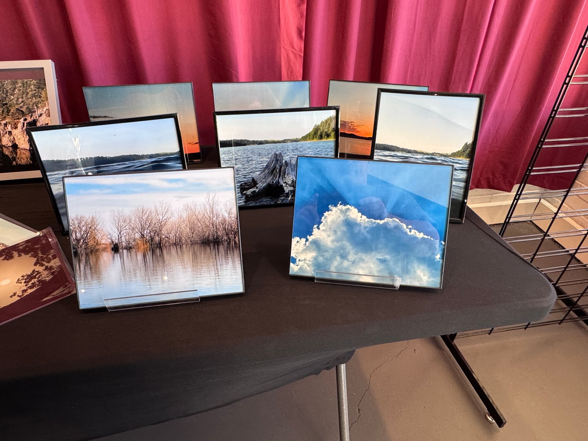 Photos of nature scenes displayed on a table. Landscapes include water, clouds, and sunsets. Black frames.