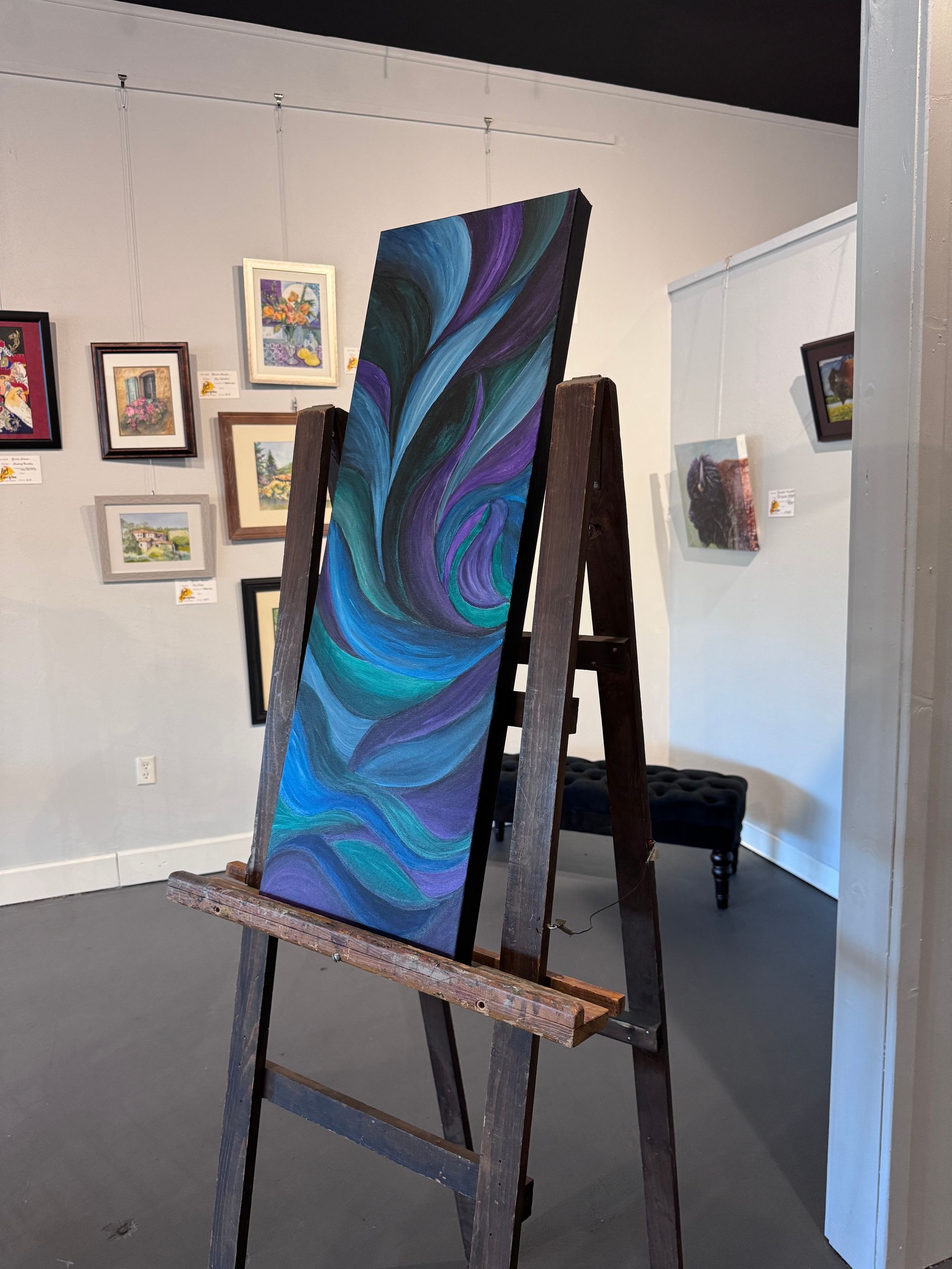 Abstract painting on an easel in a gallery, featuring blue and purple swirling patterns.