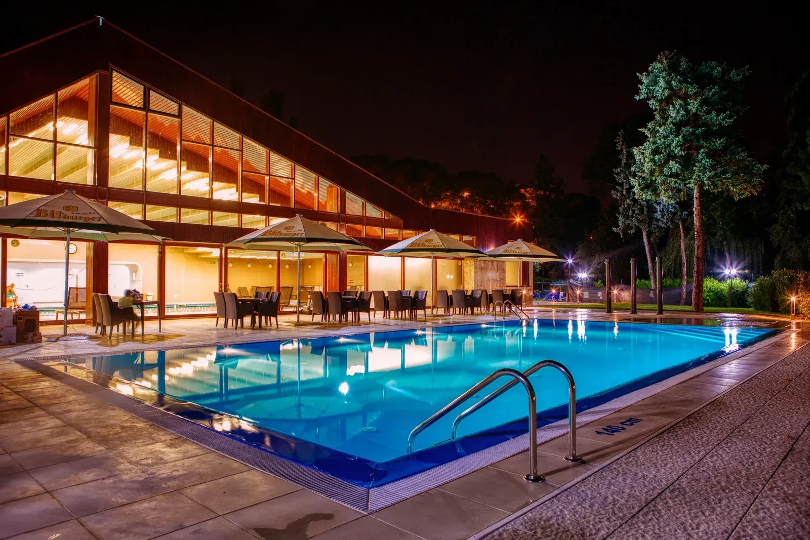 A large swimming pool is lit up at night in front of a building.