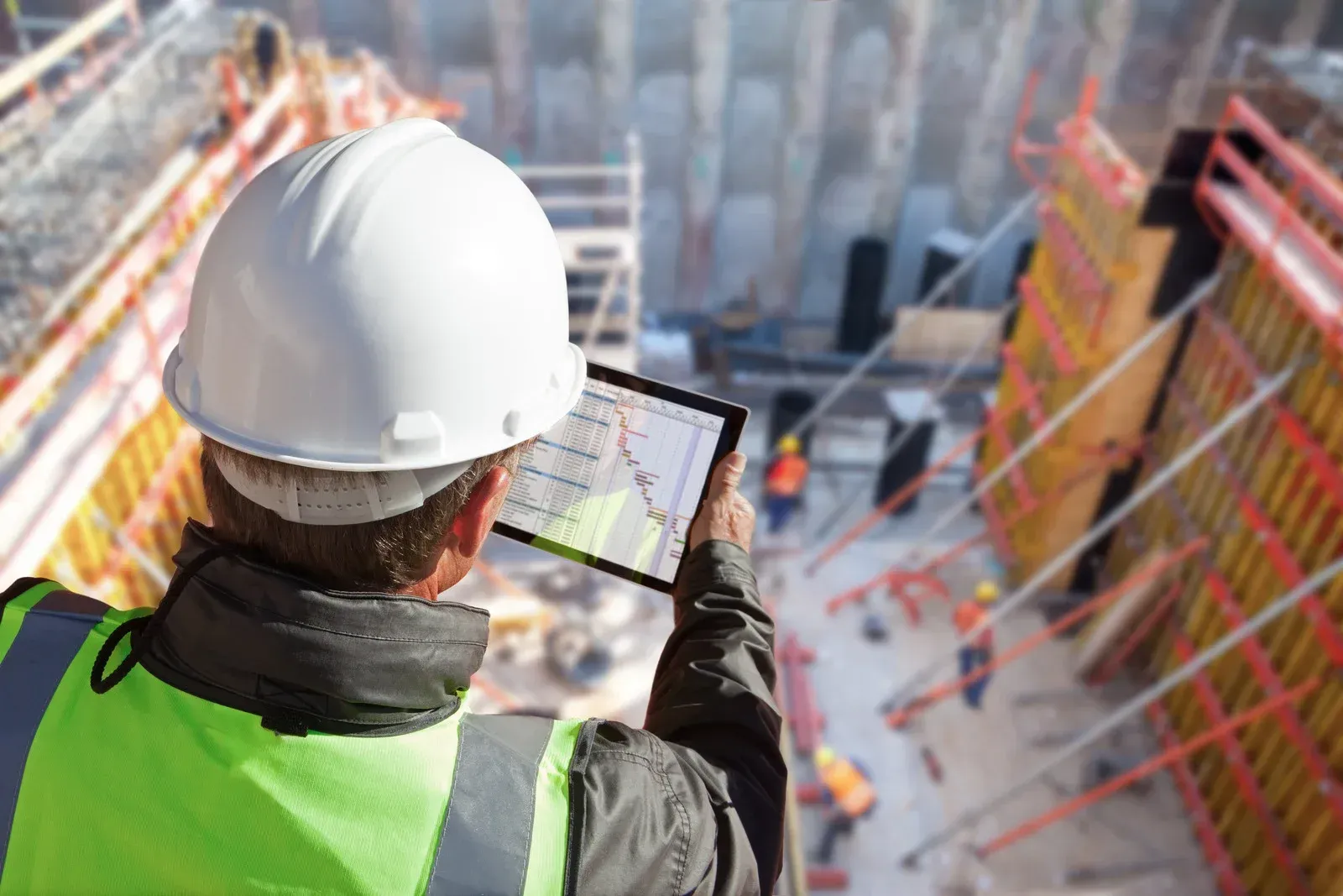 A construction worker is looking at a tablet at a construction site.