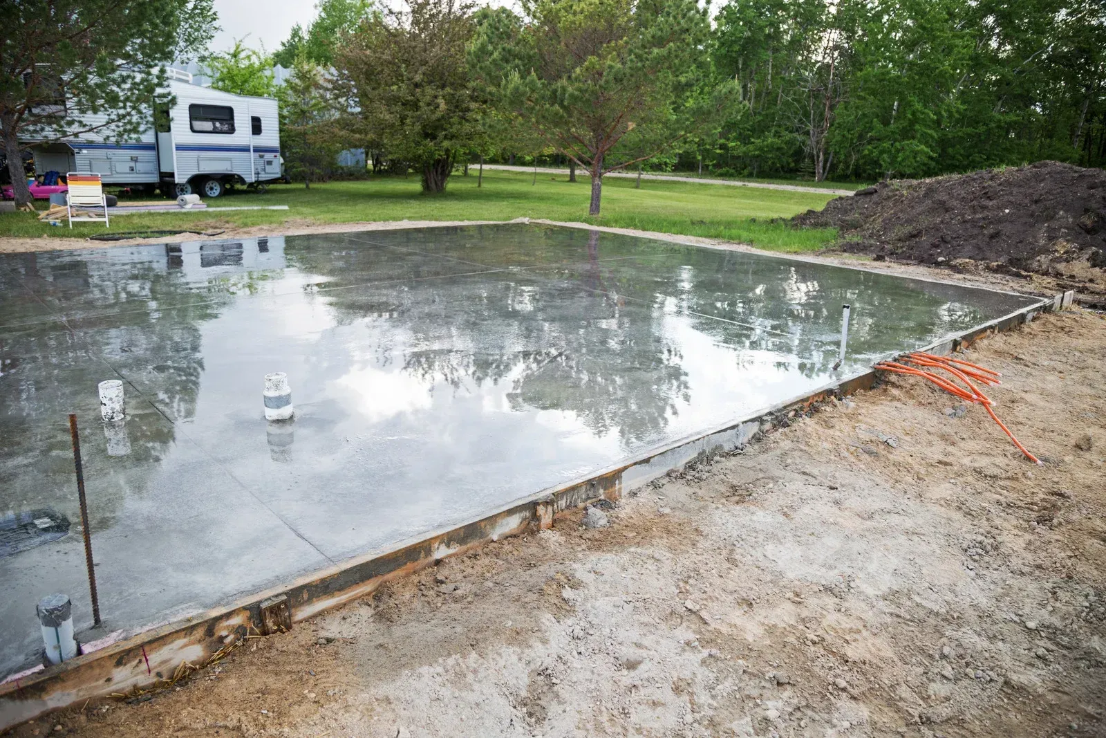 A concrete foundation is being built in a yard with a trailer parked in the background.