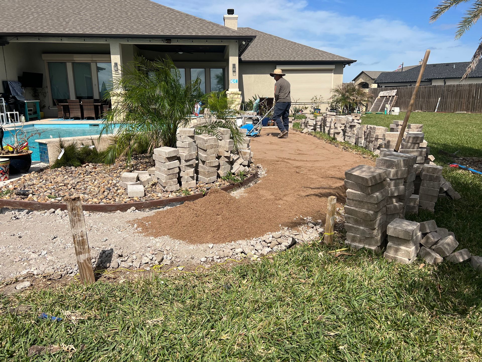 A man is walking down a dirt path in front of a house.