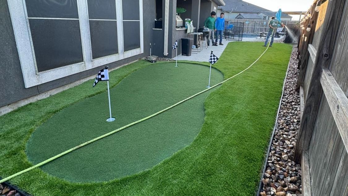 There is a putting green in the backyard of a house.