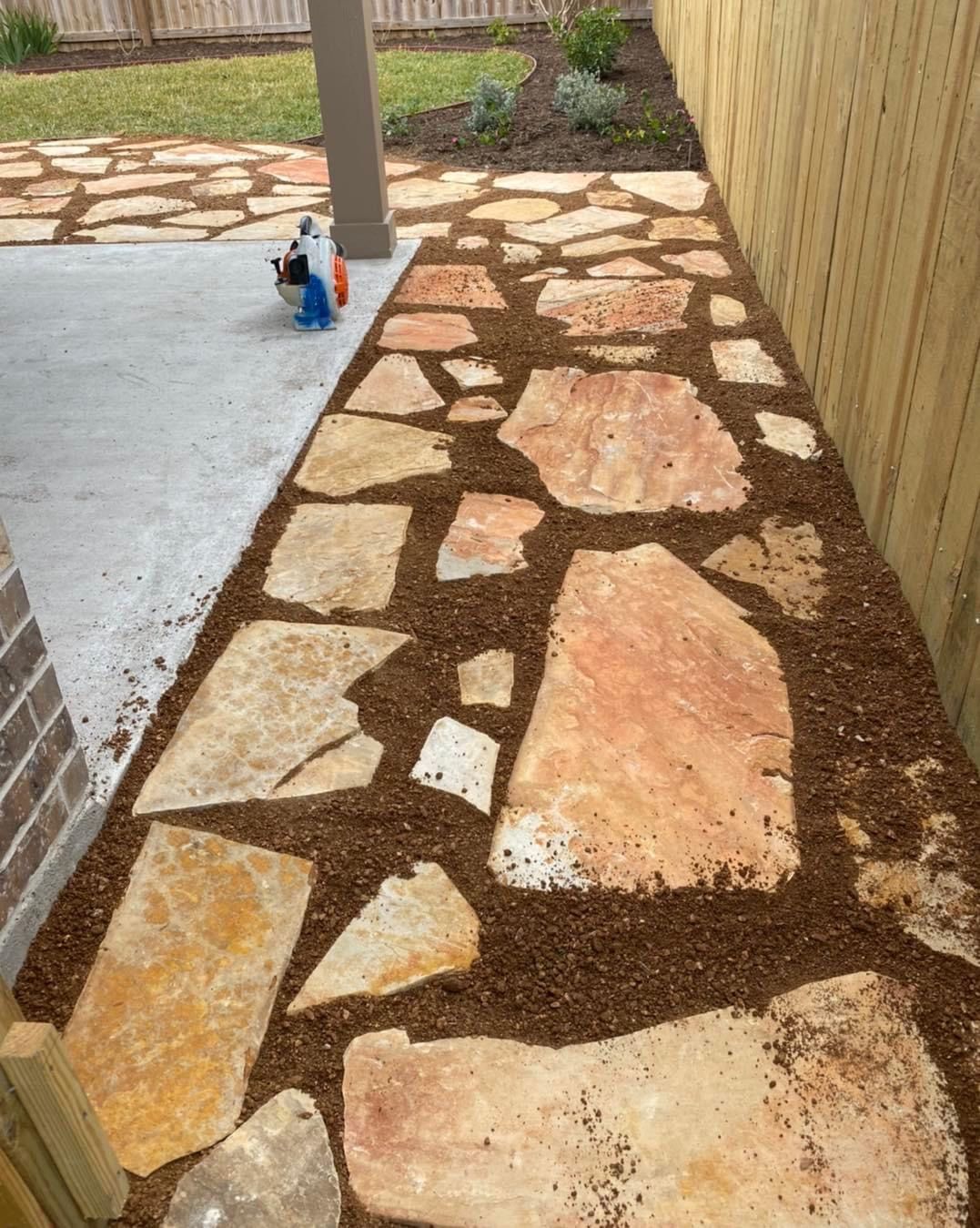 A stone walkway leading to a patio with a wooden fence in the background.