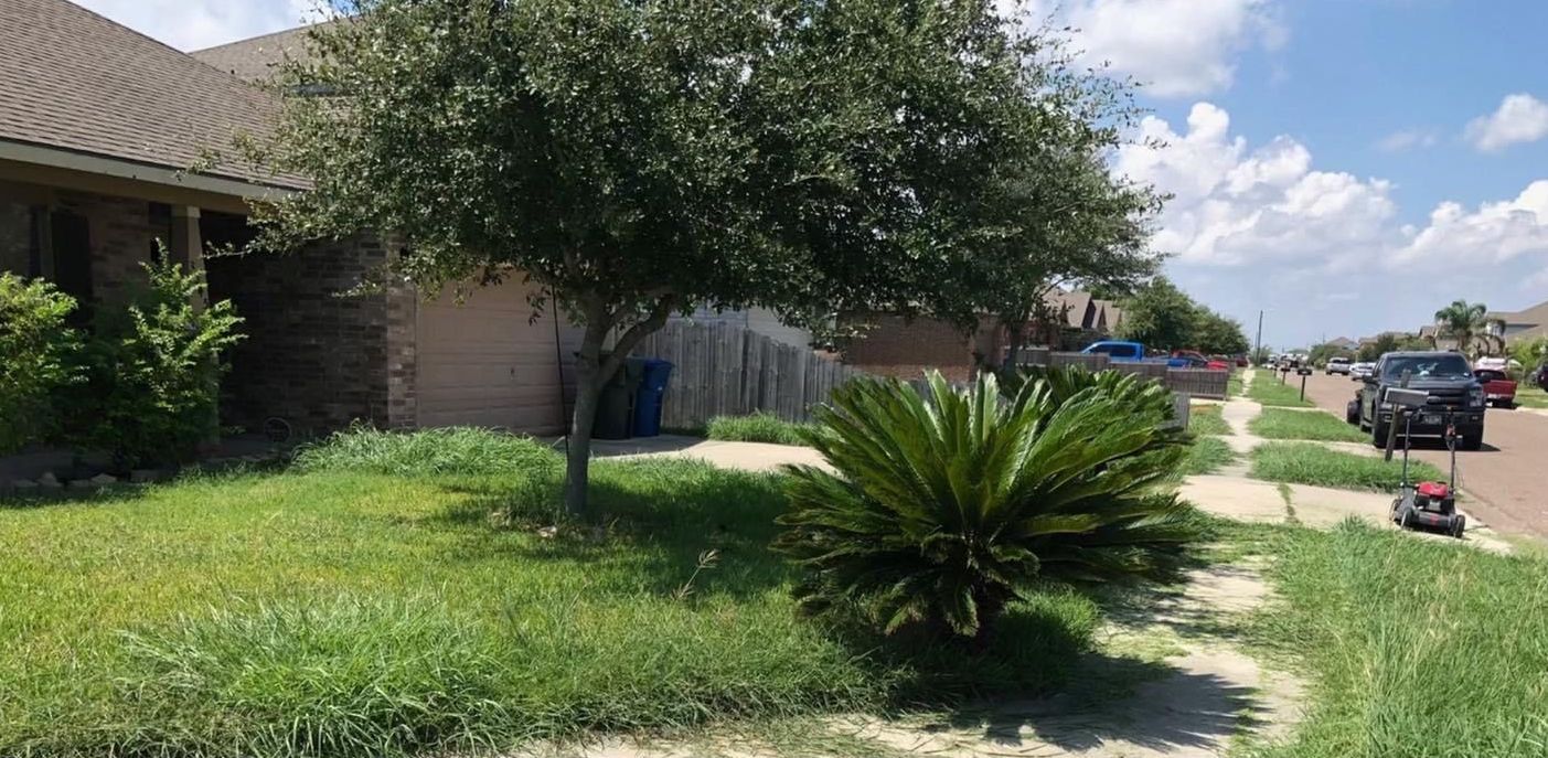 A lawn mower is cutting the grass in front of a house.