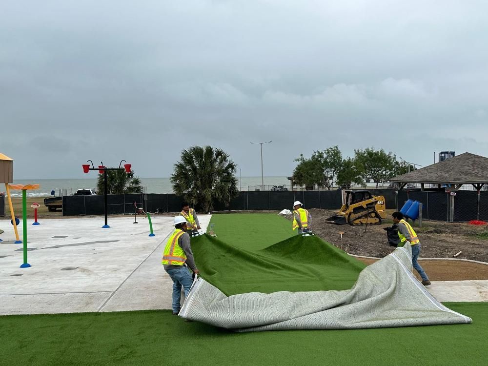 A group of construction workers are laying artificial grass on a concrete surface.