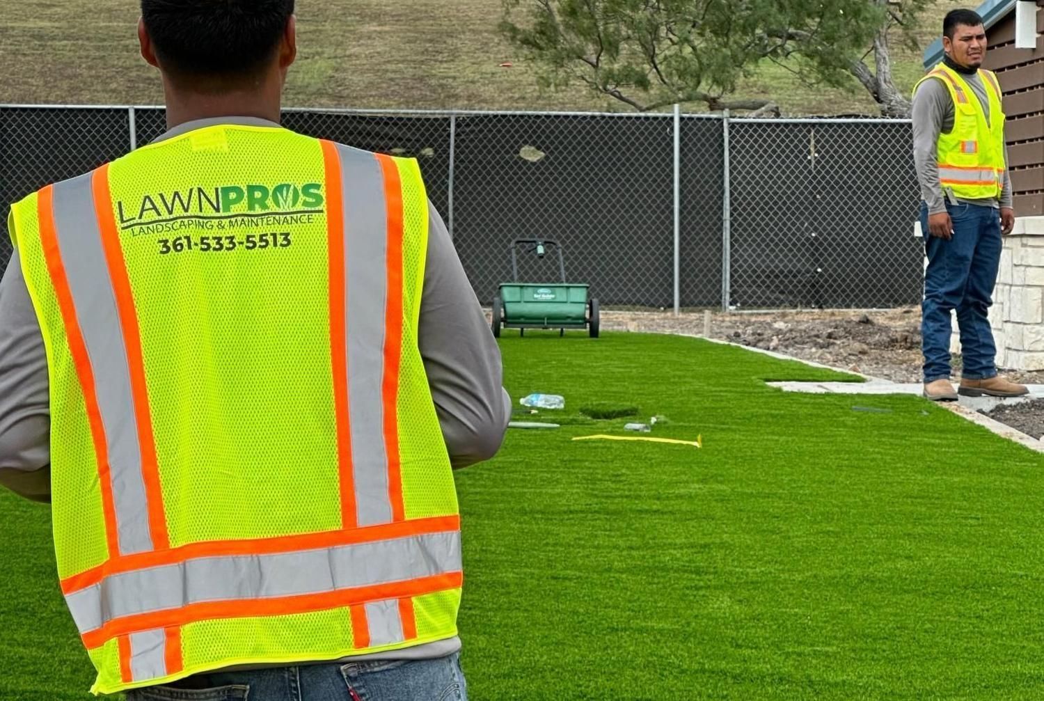 A man in a yellow vest is standing in front of artificial grass