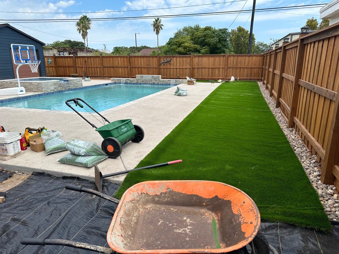 A wheelbarrow filled with dirt is sitting in a backyard next to a pool.