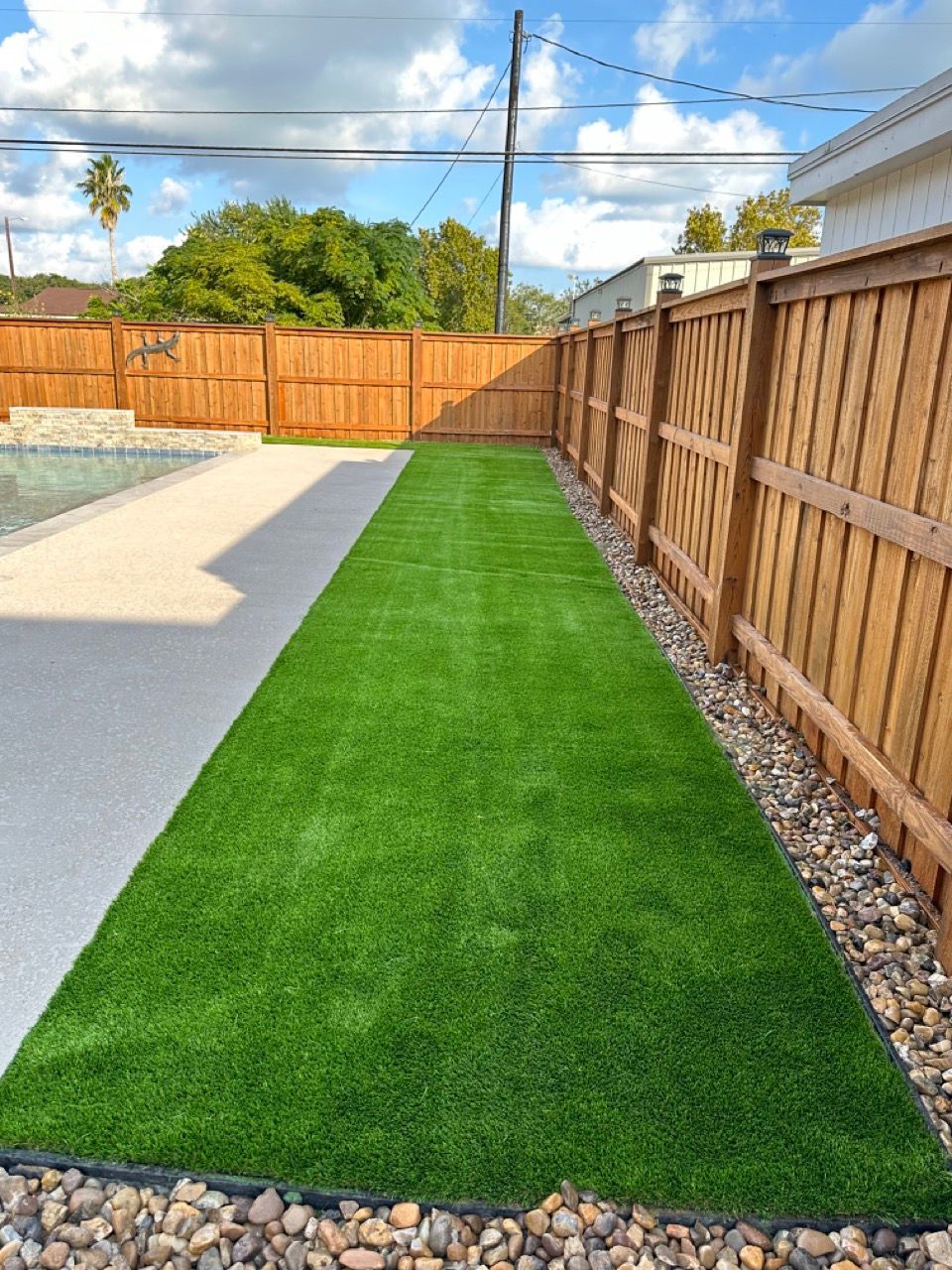 A lawn with a wooden fence and a pool in the background.