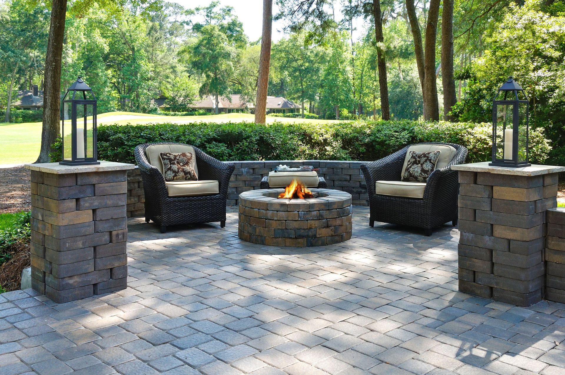 Patio with a stone fire pit, seating, and lantern posts in a garden setting.