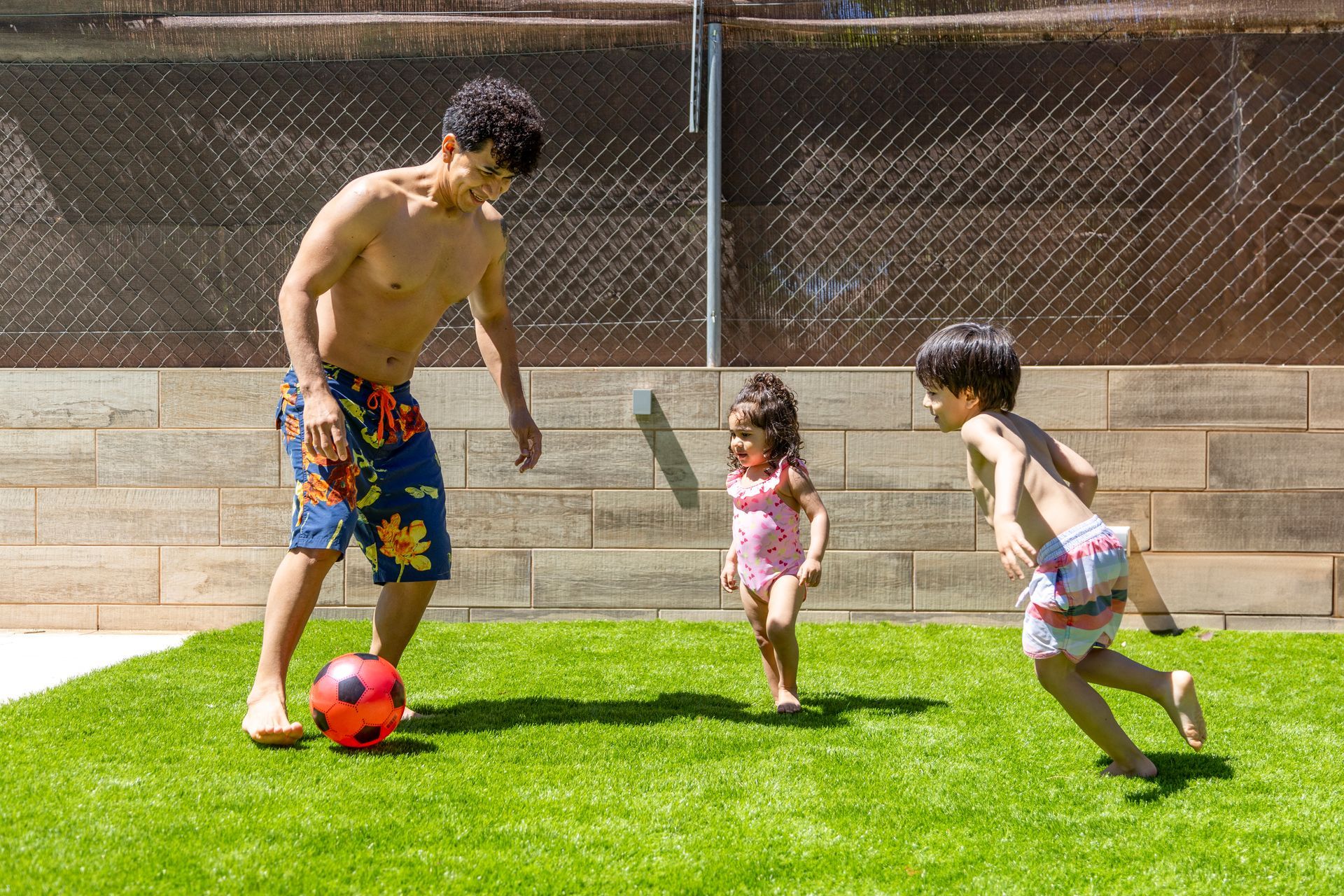 Father playing soccer with two small children on artificial grass.