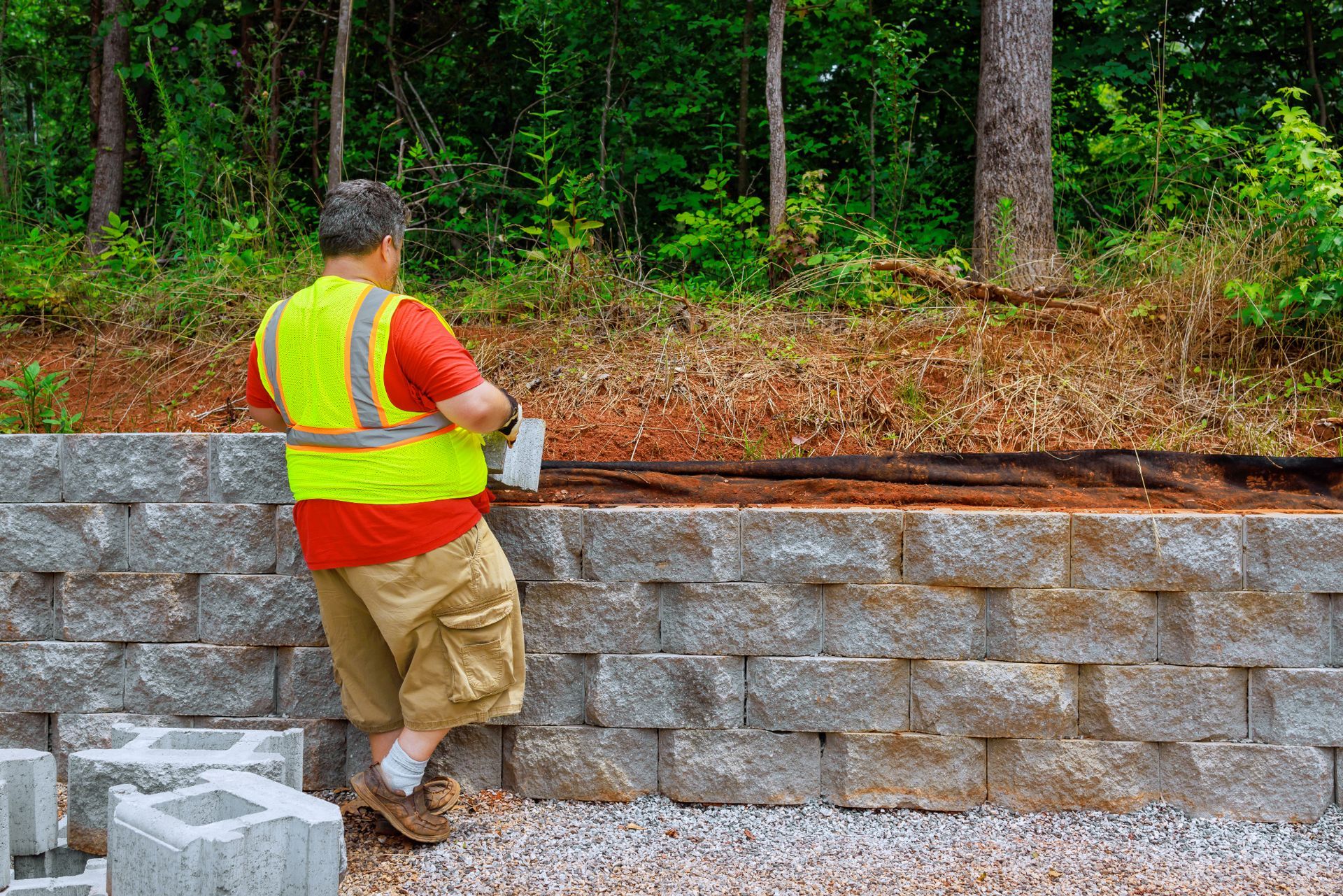 A man in a yellow vest is standing next to a brick wall.