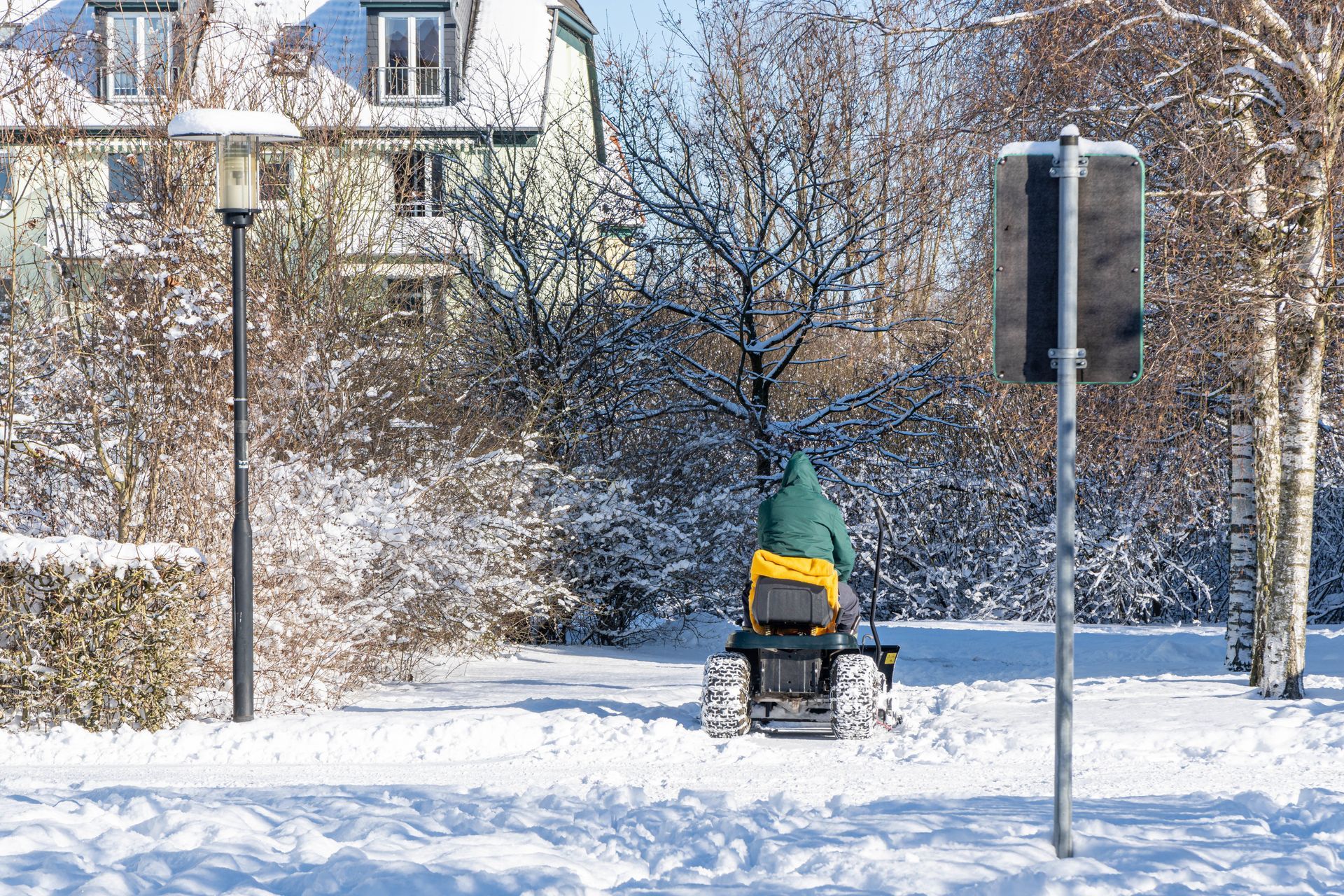 Person on snow removal machine clears path in snowy park.