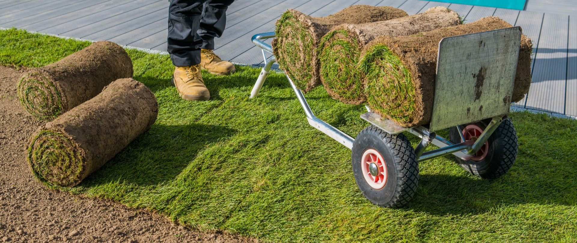 Person laying sod rolls on a green lawn with a cart.
