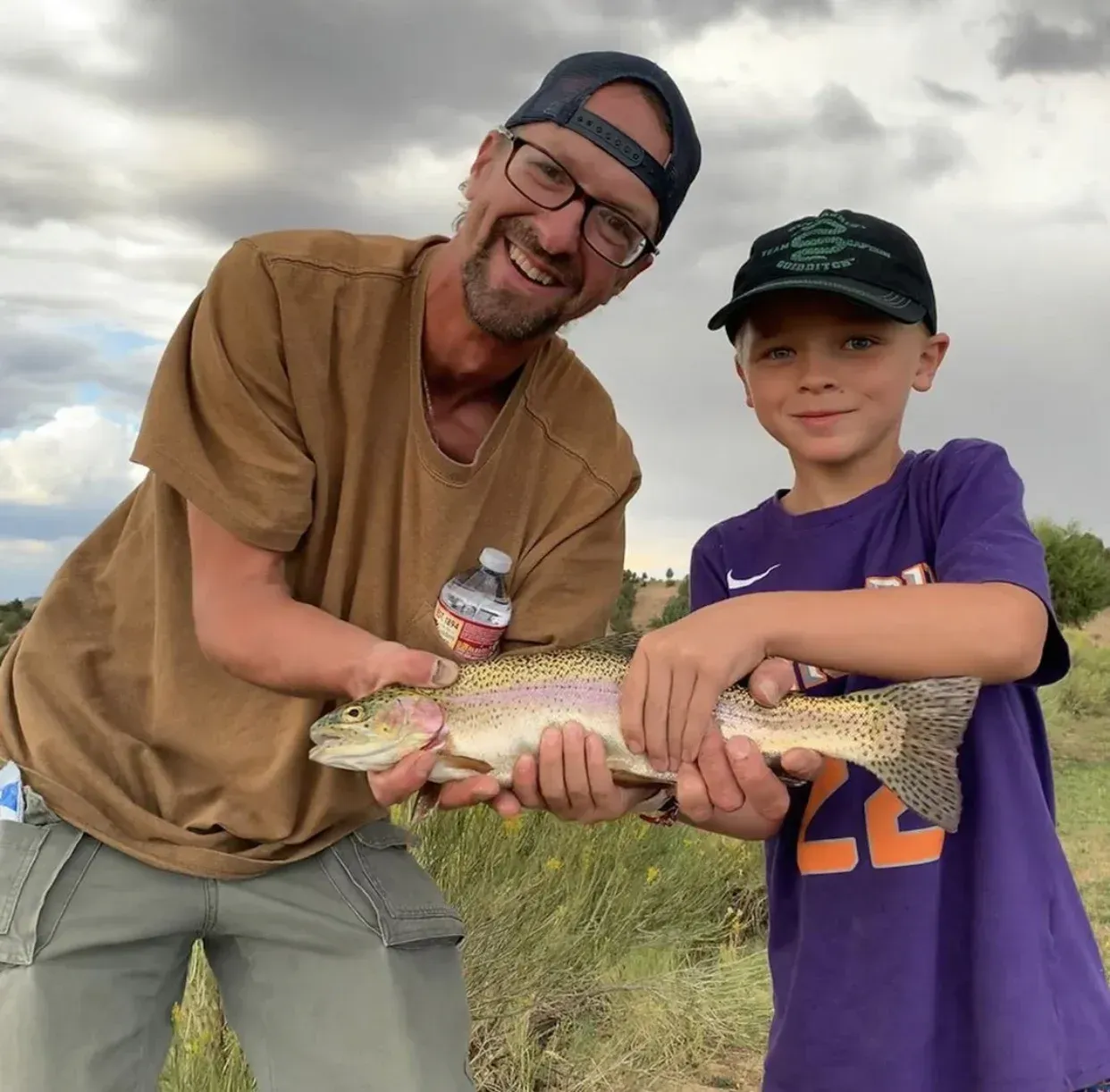 A man and a boy are holding a rainbow trout in their hands