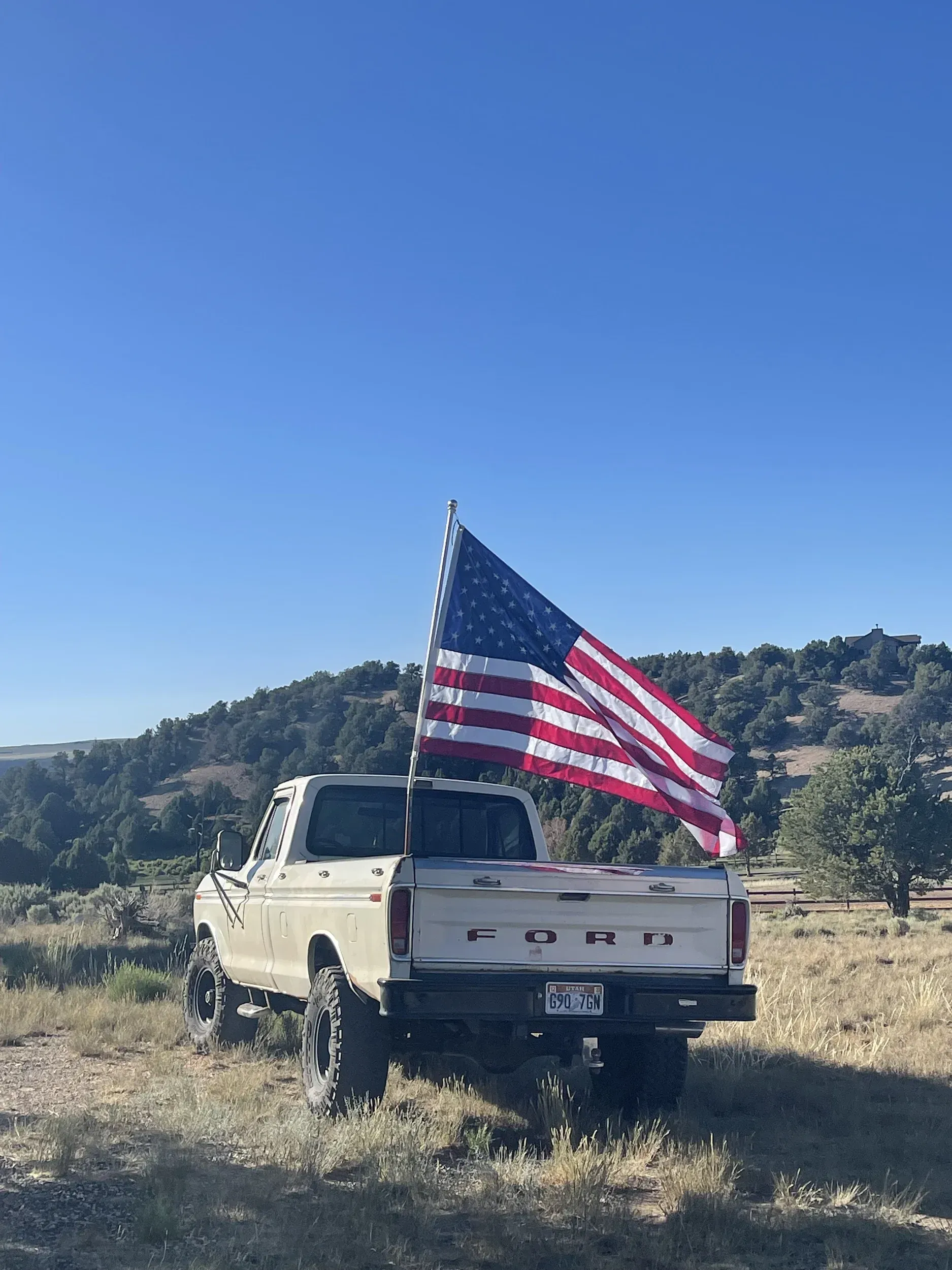 A white truck with an american flag on the back is parked in a field.