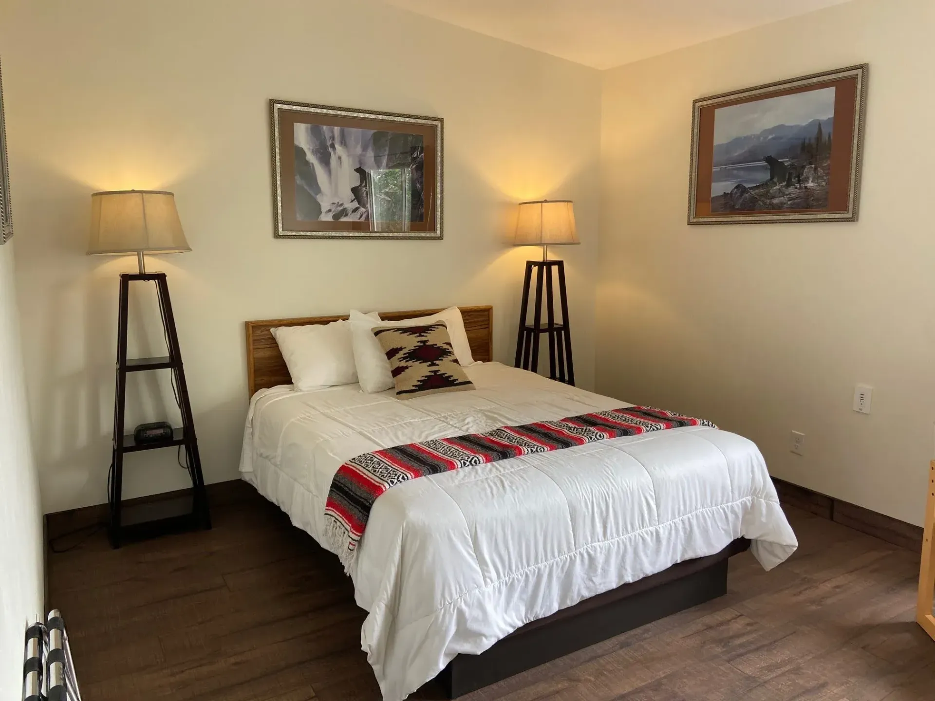 A bedroom with a bed , two lamps and two pictures on the wall.