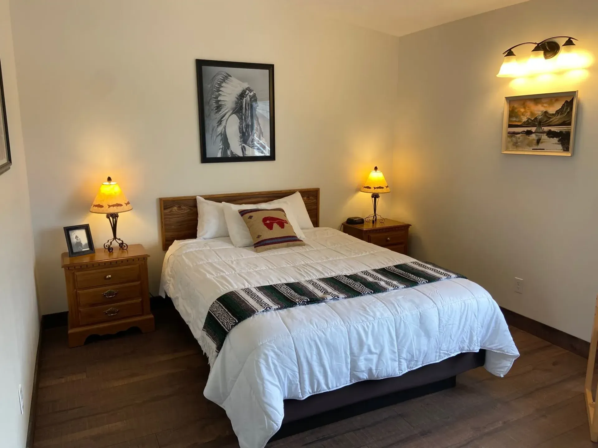 A bedroom with a bed , nightstands , lamps and a picture on the wall.