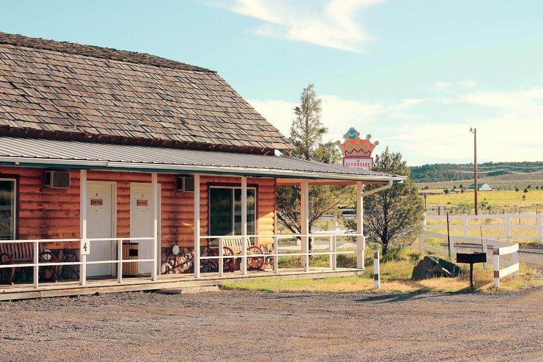 A small wooden house with a porch in the middle of a dirt field.
