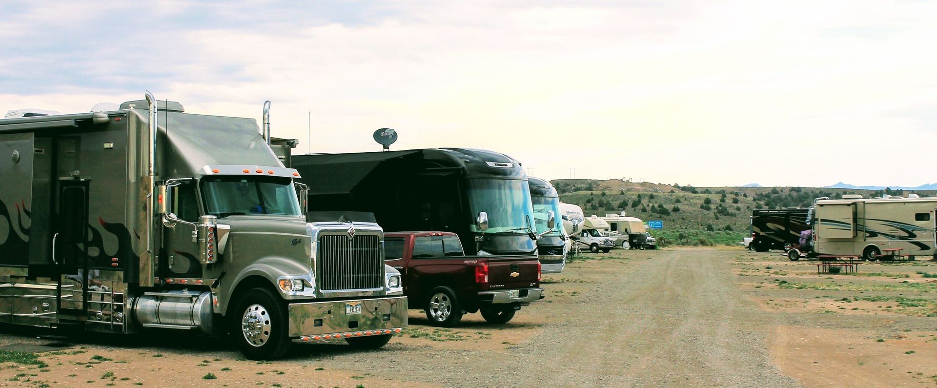 A row of rvs are parked in a dirt lot.