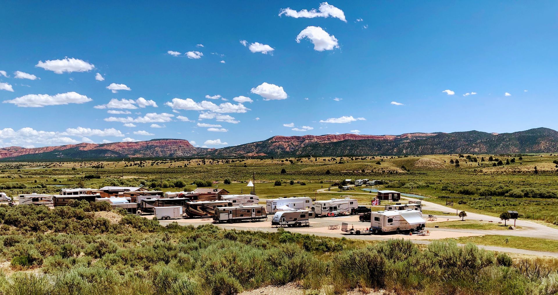 A group of rvs are parked in a field with mountains in the background.