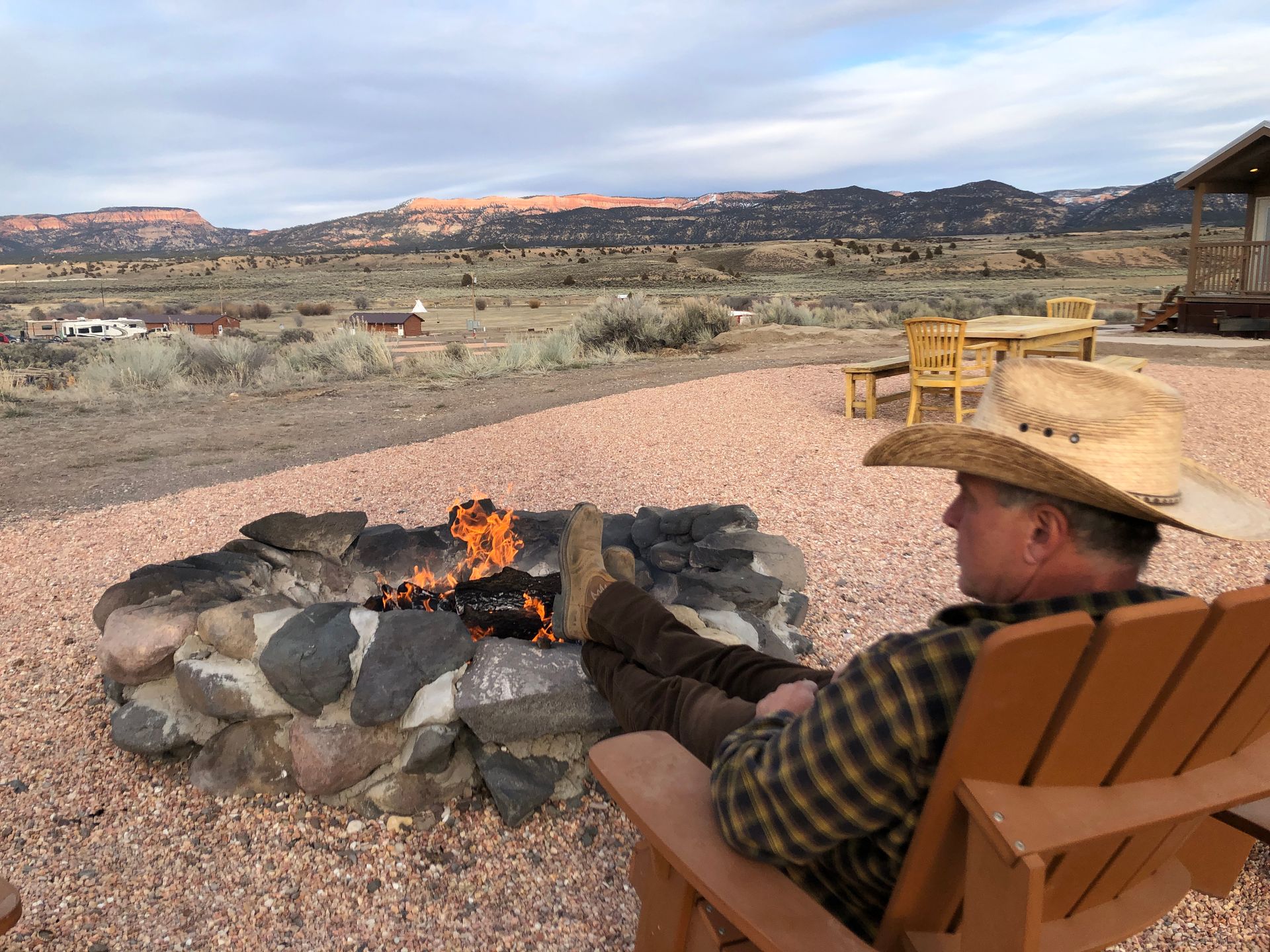 A man in a cowboy hat is sitting in a chair near a fire pit.