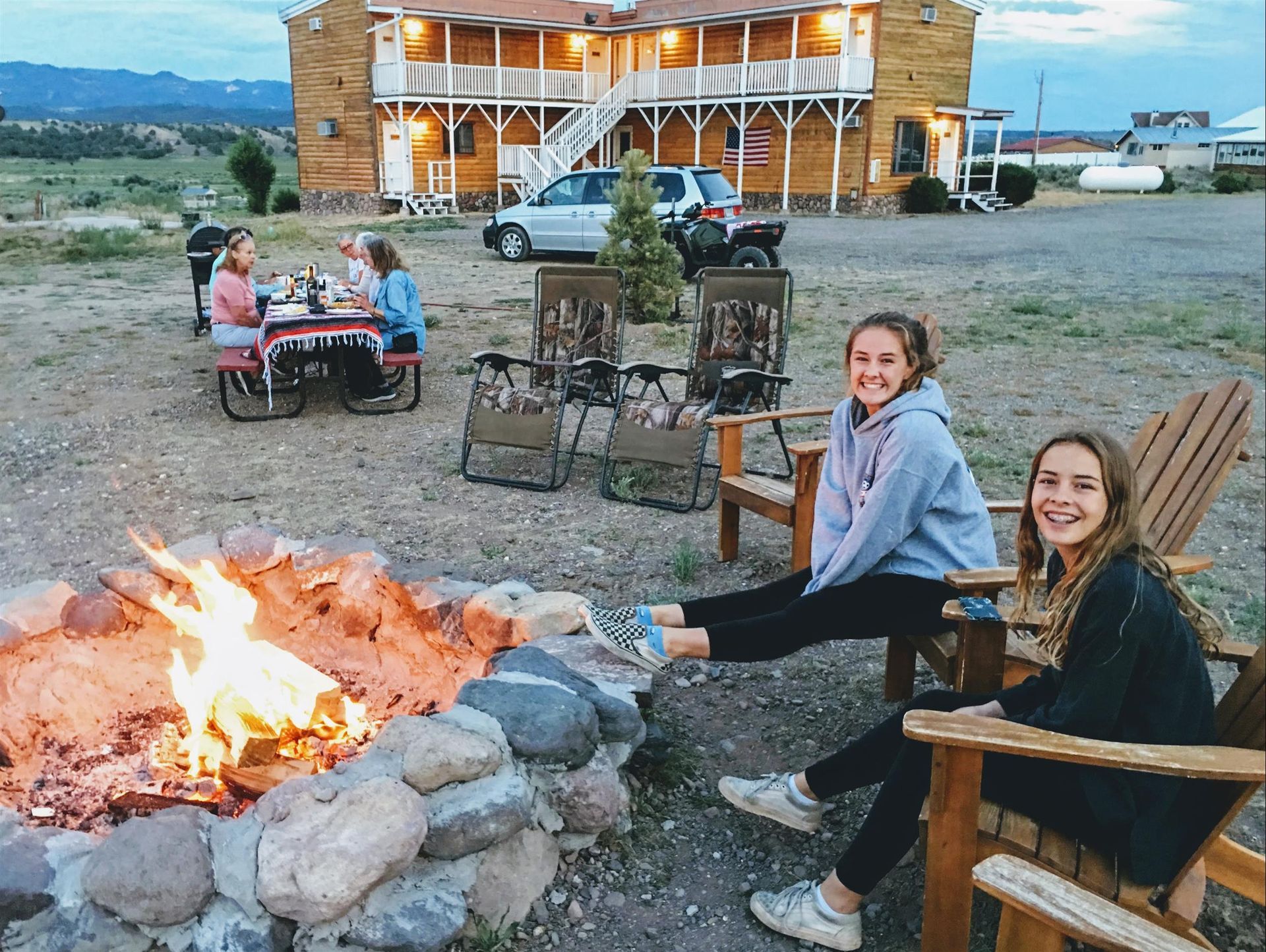 A group of people are sitting around a fire pit in front of a building.