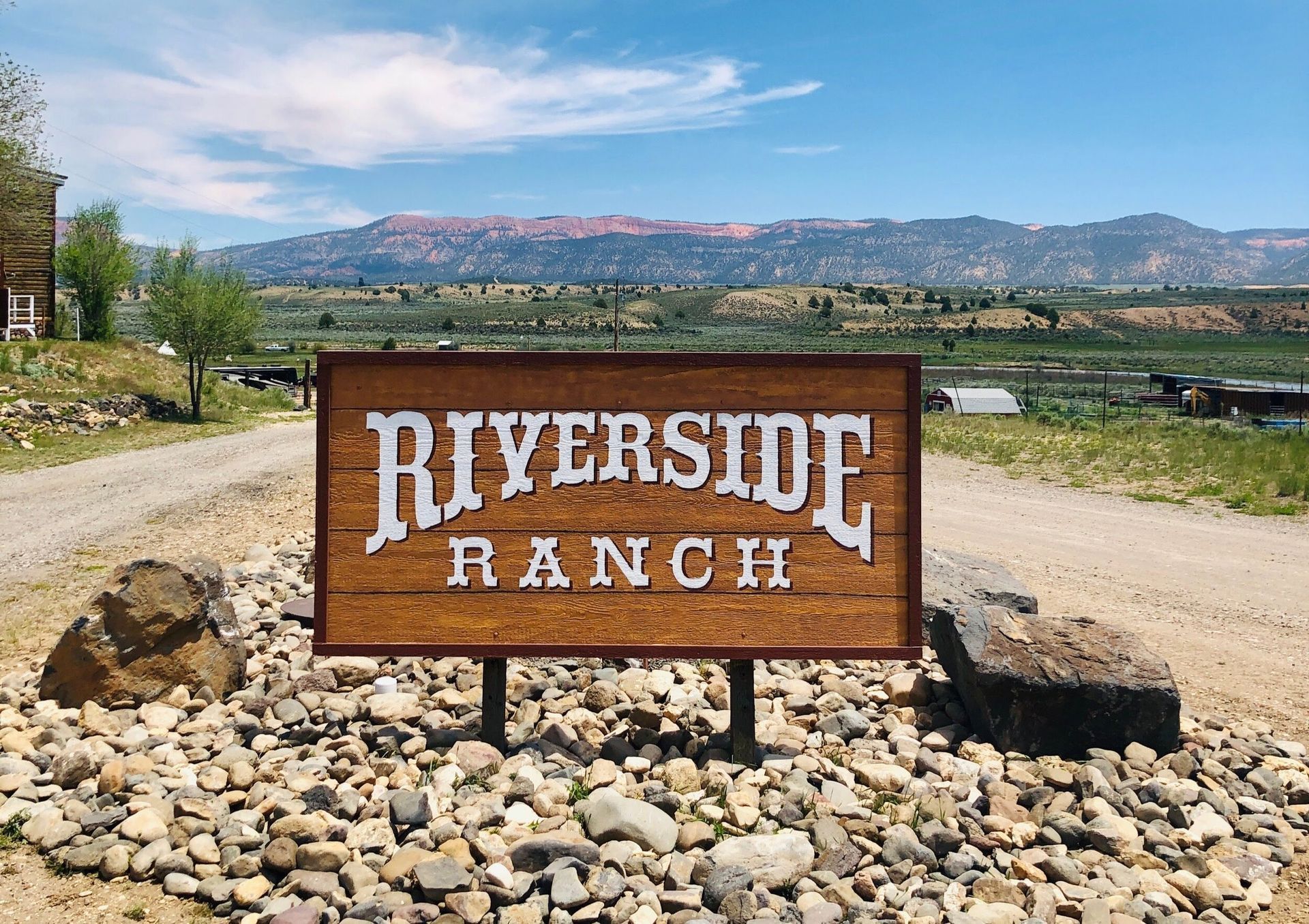 A sign for riverside ranch is sitting on top of a pile of rocks.