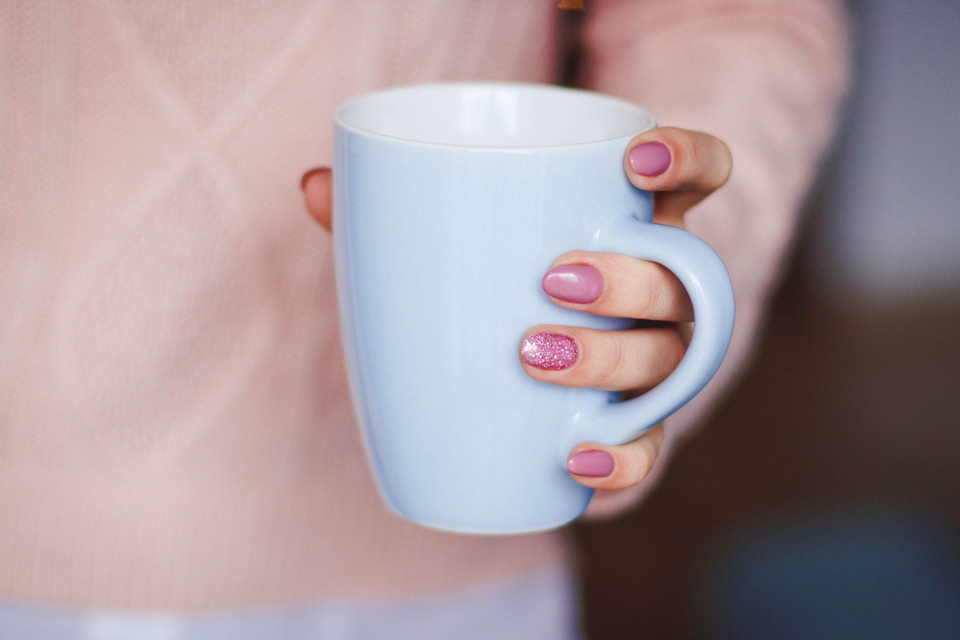 A woman with pink nails is holding a blue cup of coffee.