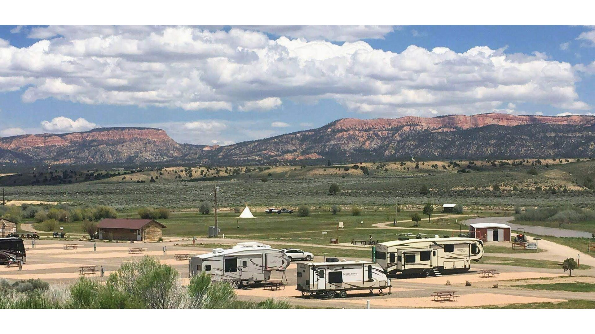 A group of rvs are parked in a field with mountains in the background.