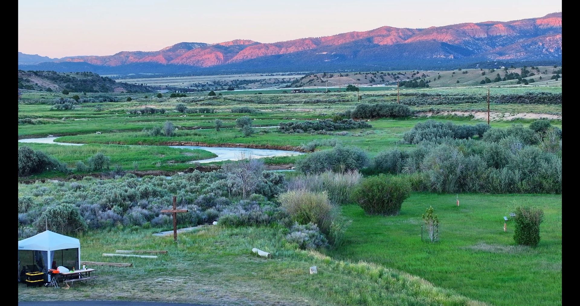 A tent is sitting in the middle of a grassy field with mountains in the background.