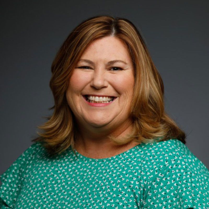 A woman in a green shirt is smiling for the camera.