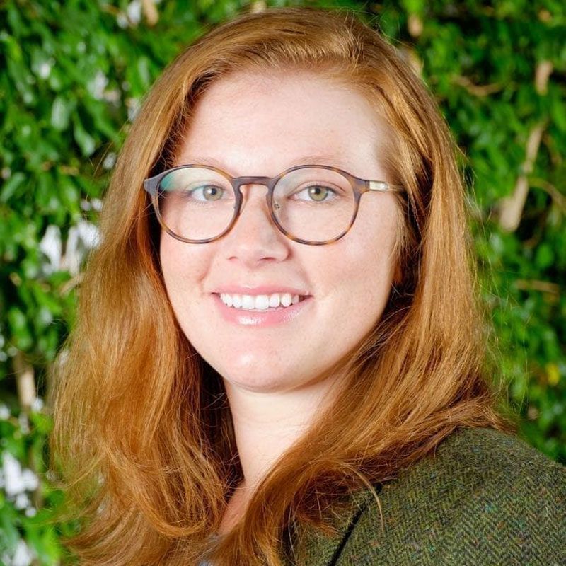 A woman with red hair and glasses is smiling for the camera.