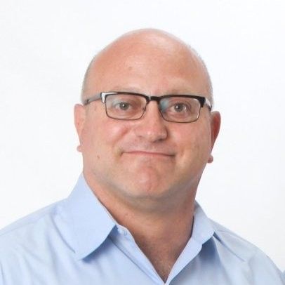 A bald man wearing glasses and a blue shirt is smiling for the camera.