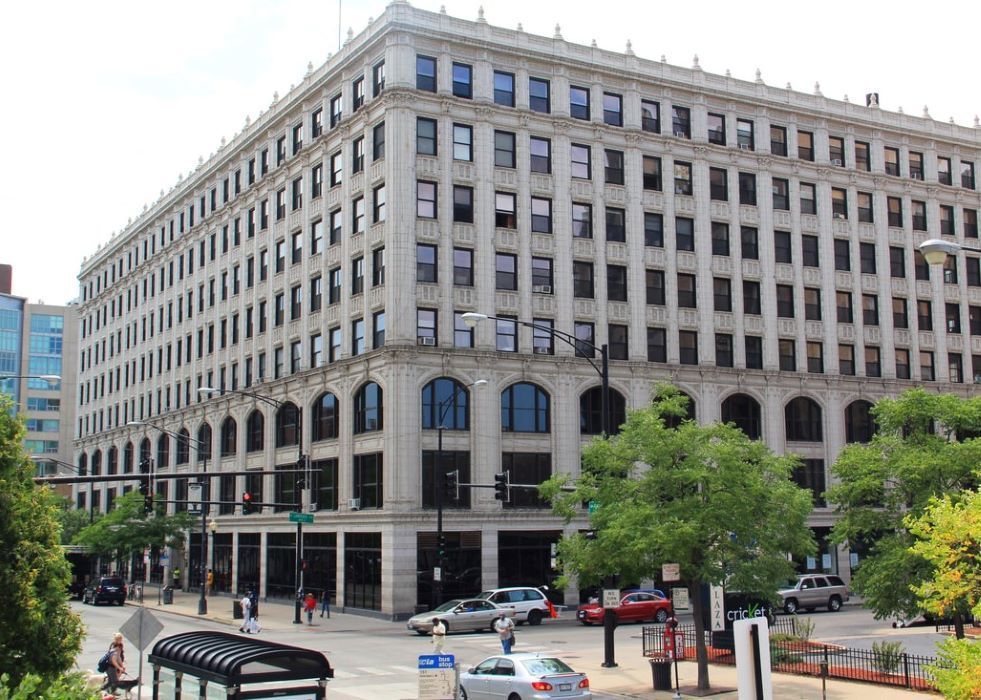A large building with a lot of windows is sitting on the corner of a city street.