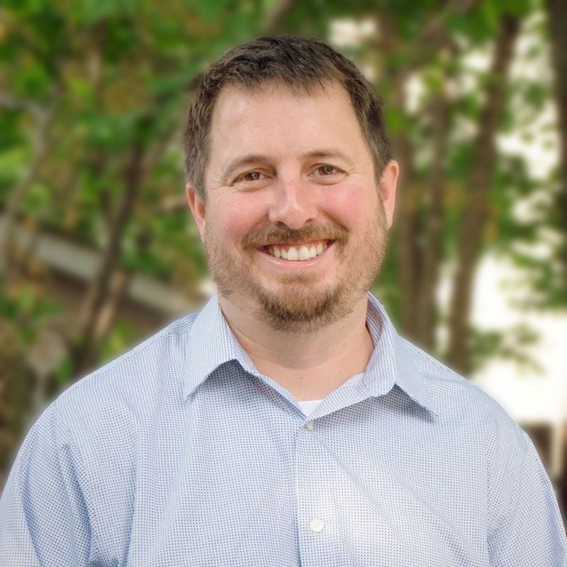 A man with a beard is smiling for the camera while wearing a blue shirt.