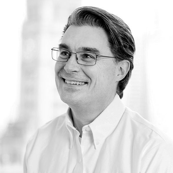 A man wearing glasses and a white shirt is smiling in a black and white photo.