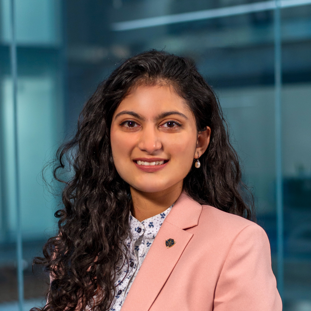 A woman wearing a pink jacket and a white shirt is smiling for the camera.