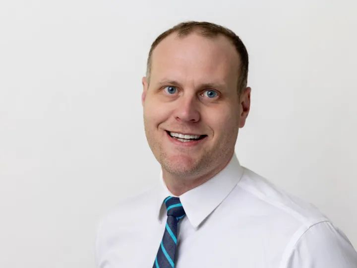 A man in a white shirt and tie is smiling for the camera.