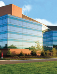 A large building with lots of windows is surrounded by grass and trees