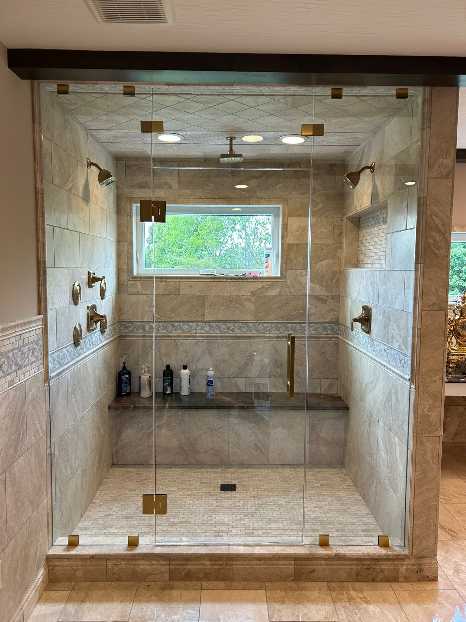 A bathroom with a walk in shower with a glass door and a window.