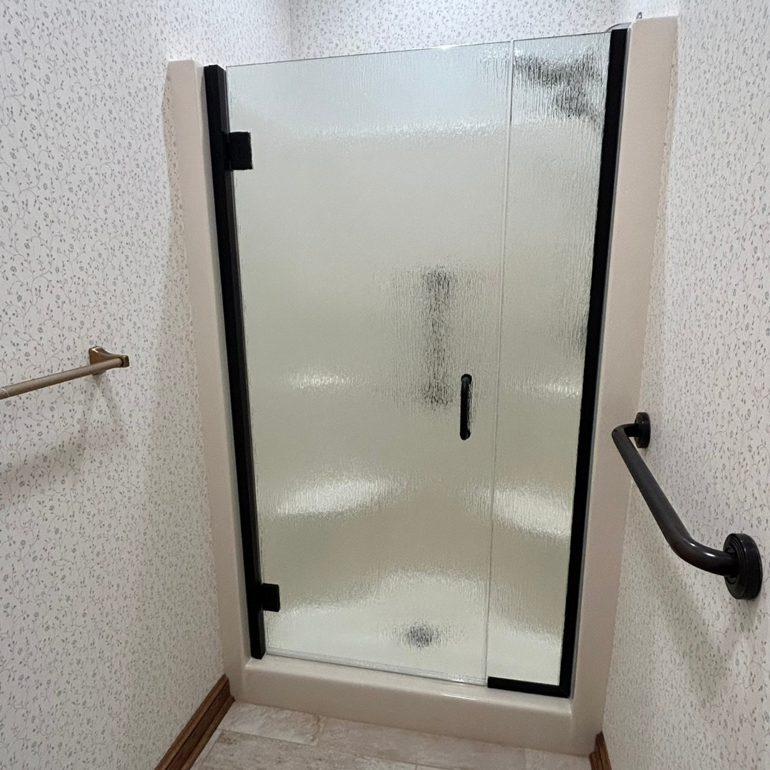 A bathroom with a glass shower door and a black handle.