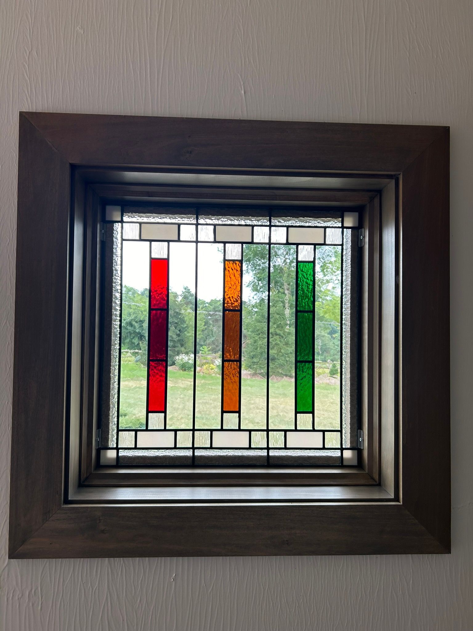 A stained glass window with a wooden frame is hanging on a wall.